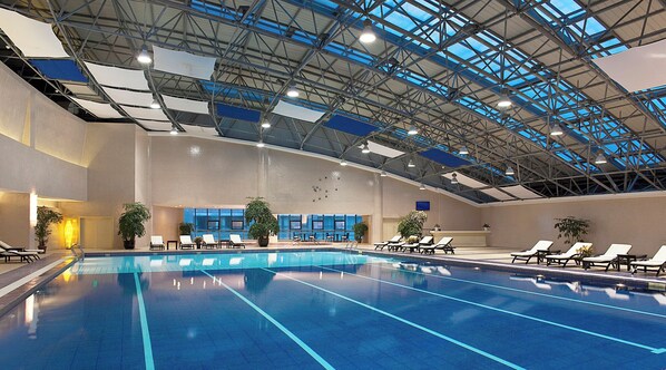 Una piscina interior con múltiples carriles, sillas de descanso y plantas en macetas.