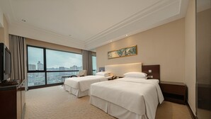 Habitación de hotel con dos camas, un ventanal con vistas a la ciudad, un cuadro en la pared y un televisor a la izquierda.