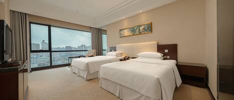 A hotel room with two beds, a large window with a city view, a painting on the wall, and a television on the left.