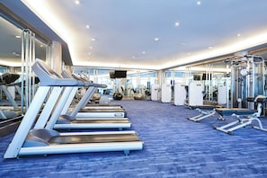 Une salle de sport équipée de tapis de course, d’appareils de musculation et recouverte d’une moquette bleue.
