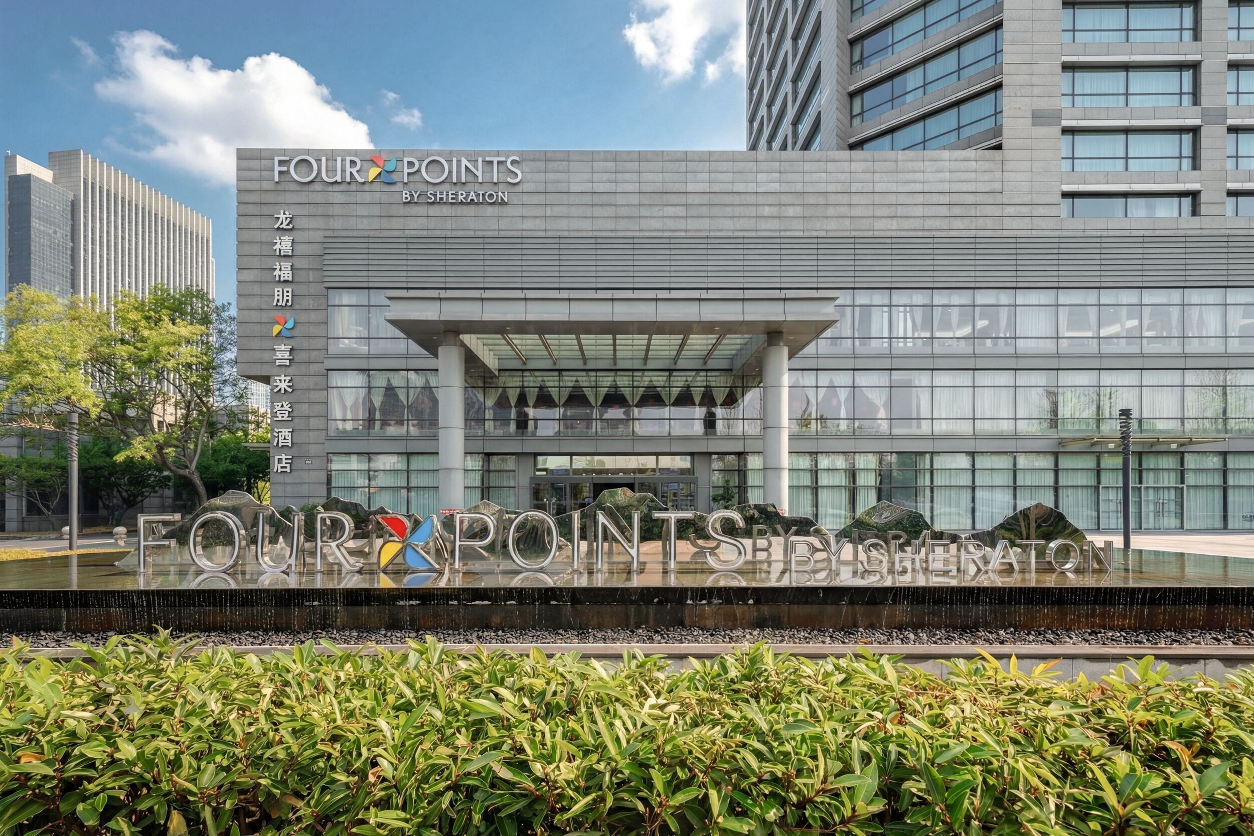 A modern building with a sign reading 'FOUR POINTS BY SHERATON' and a large entrance with a glass canopy.