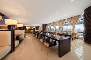 Un lobby moderno de hotel con un mostrador de recepción amplio, varias zonas de estar y grandes ventanales con vistas a la ciudad.