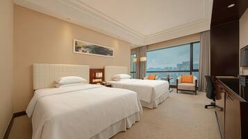 A hotel room with two beds, a desk, a chair, and a large window with a city view.