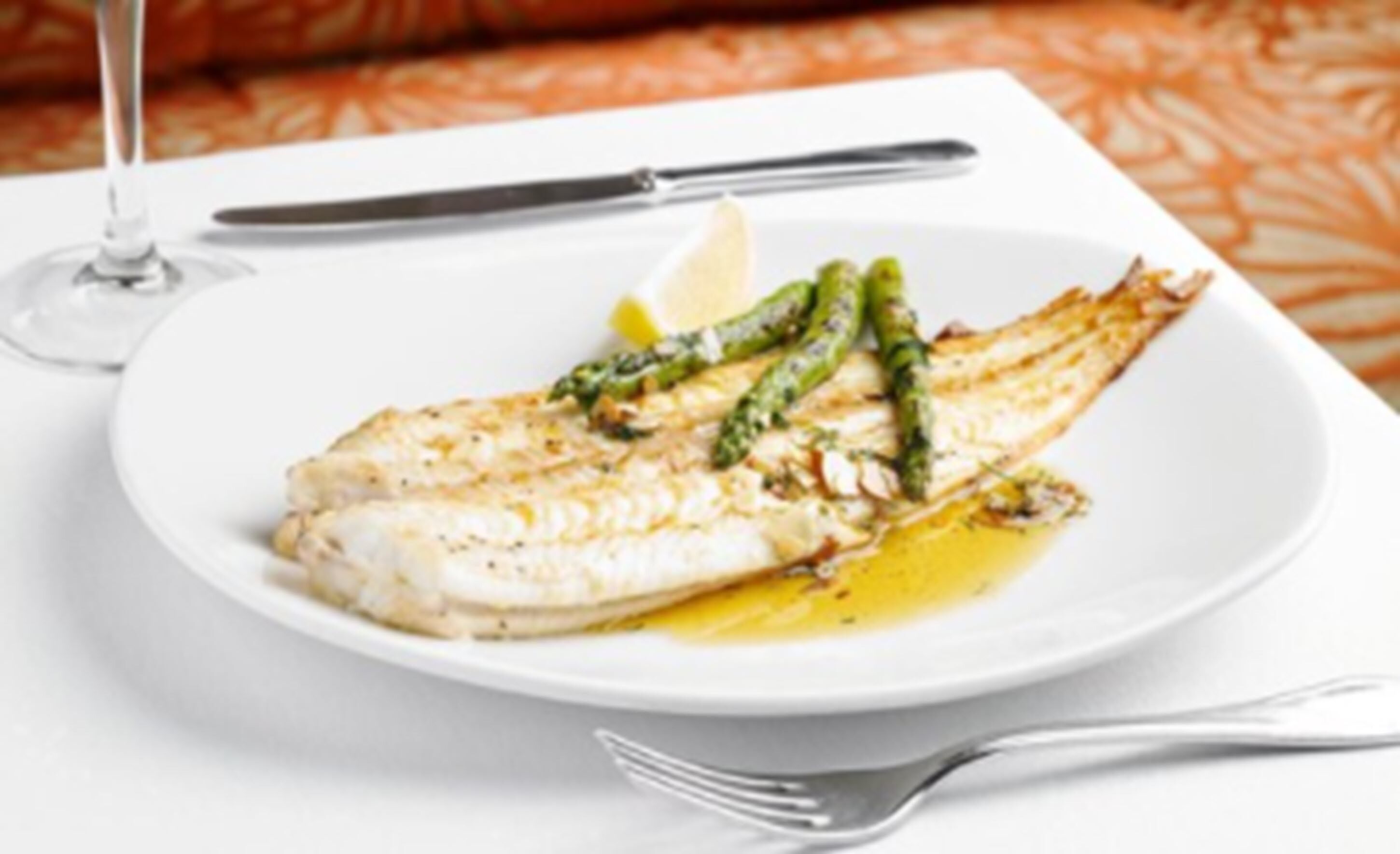 A plate of fish with asparagus and lemon on a white tablecloth.