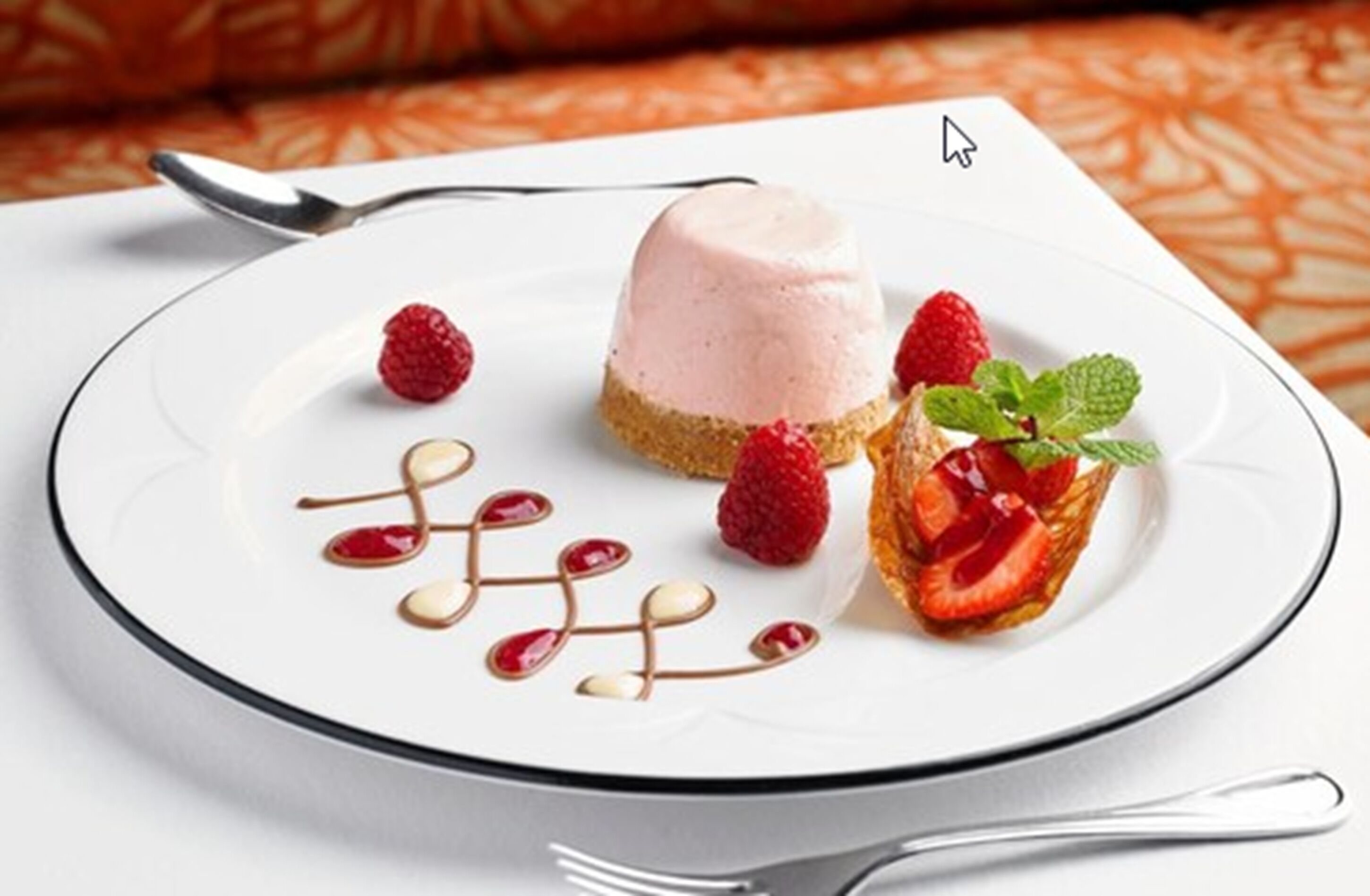 A dessert plate with a scoop of ice cream, raspberries, and a strawberry tart, accompanied by a spoon and a fork.