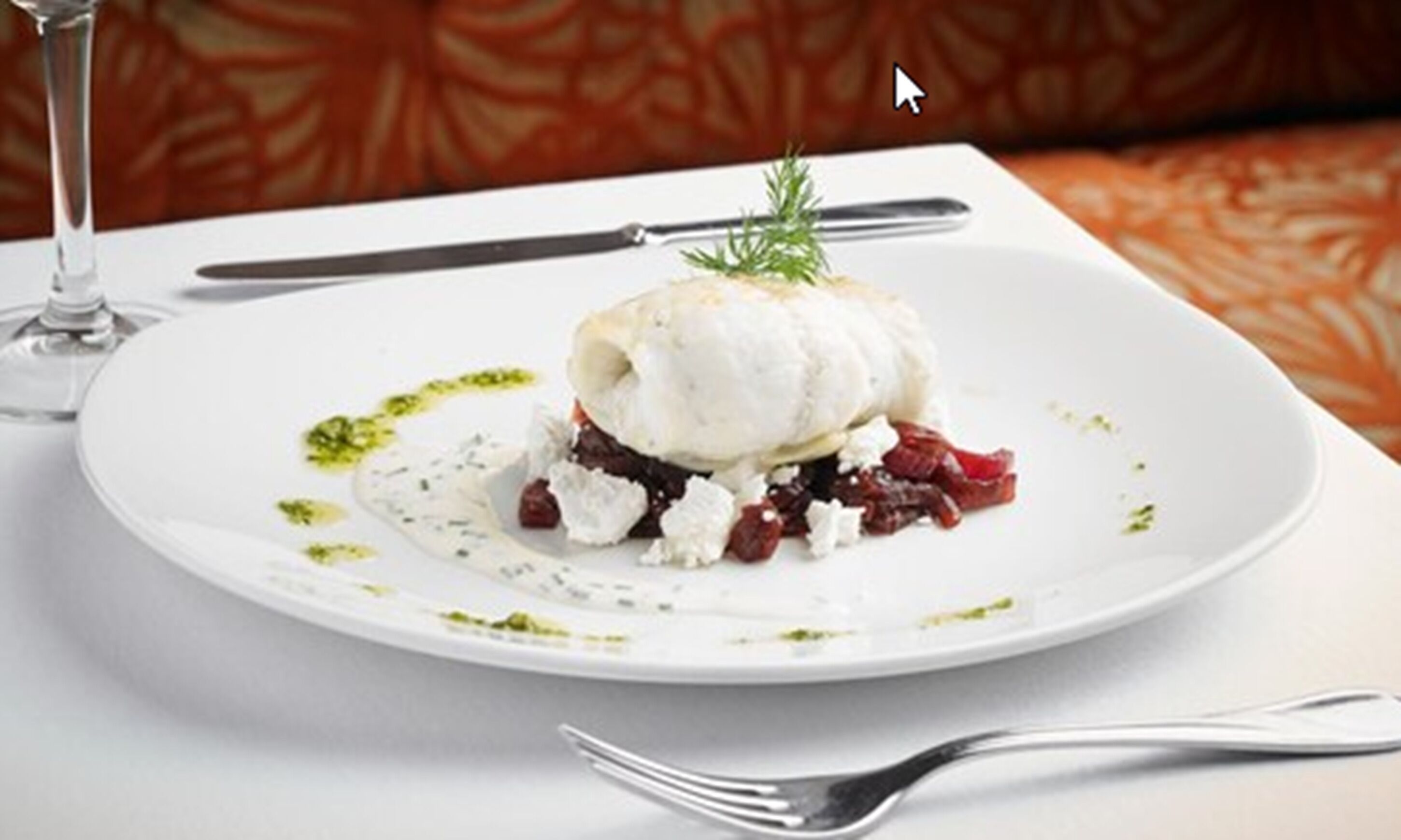 Een wit bord met een wit gerecht, mogelijk vis of vlees, versierd met kruiden en een rozemarijnstengel.
