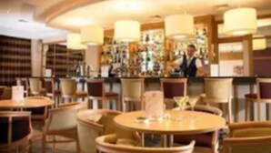 A bar area with round tables and chairs, a bartender, and shelves with bottles. - Sneem Hotel (Sneem)
