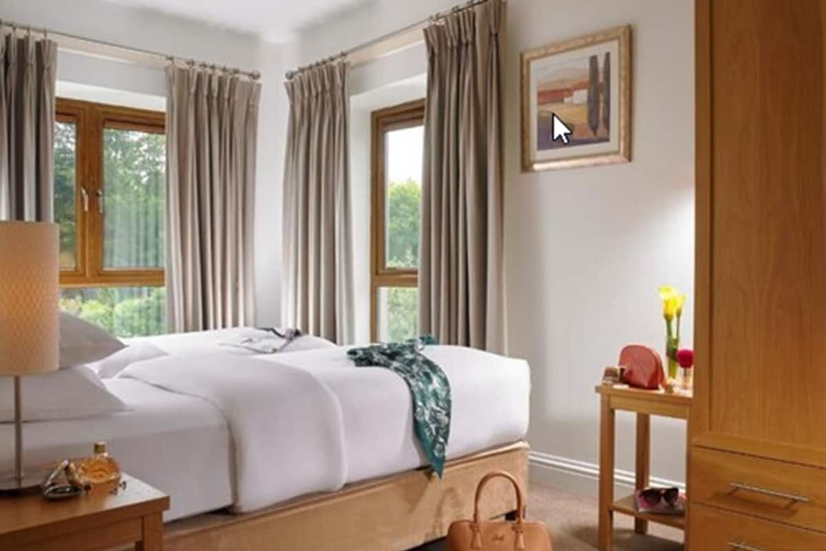 A hotel room with a bed, a nightstand, a lamp, a wooden wardrobe, and a window with curtains.