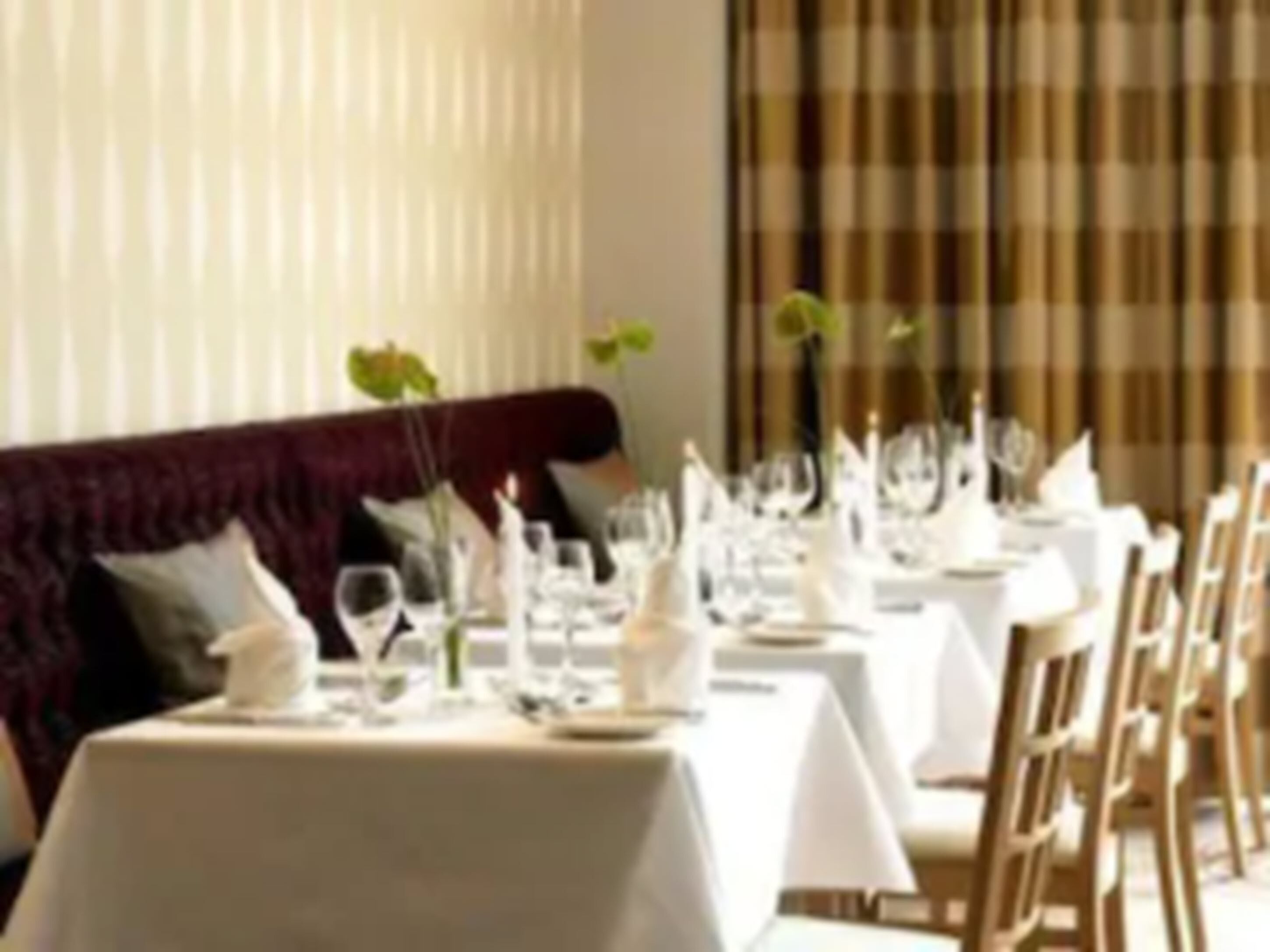 A restaurant with tables set for dining, featuring a red upholstered bench and white tablecloths.