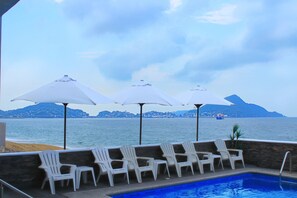 Una piscina al aire libre, sombrillas, sillones reclinables de piscina