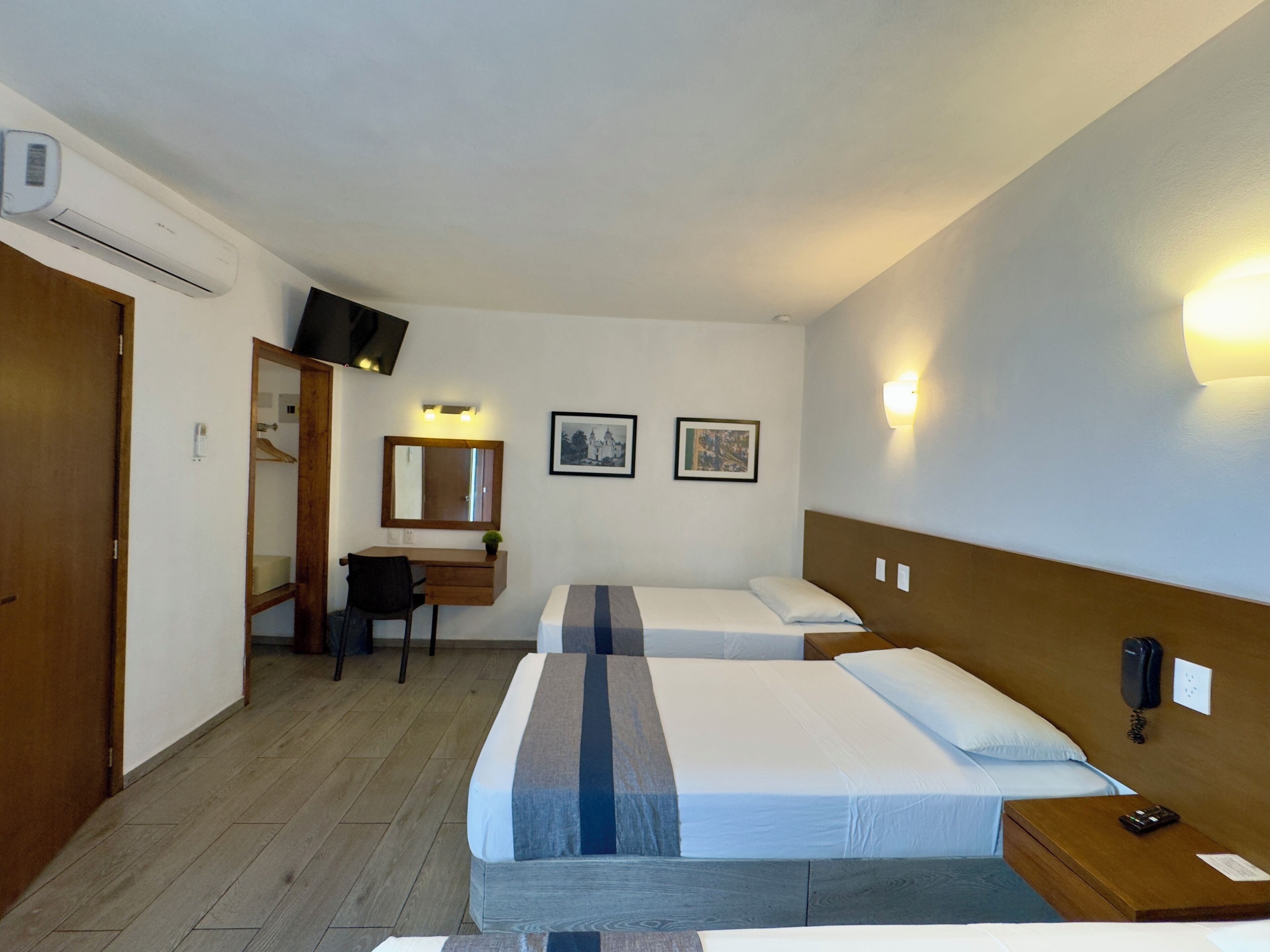 Une chambre d’hôtel avec deux lits, un bureau, une chaise, un miroir et un téléphone fixé au mur.