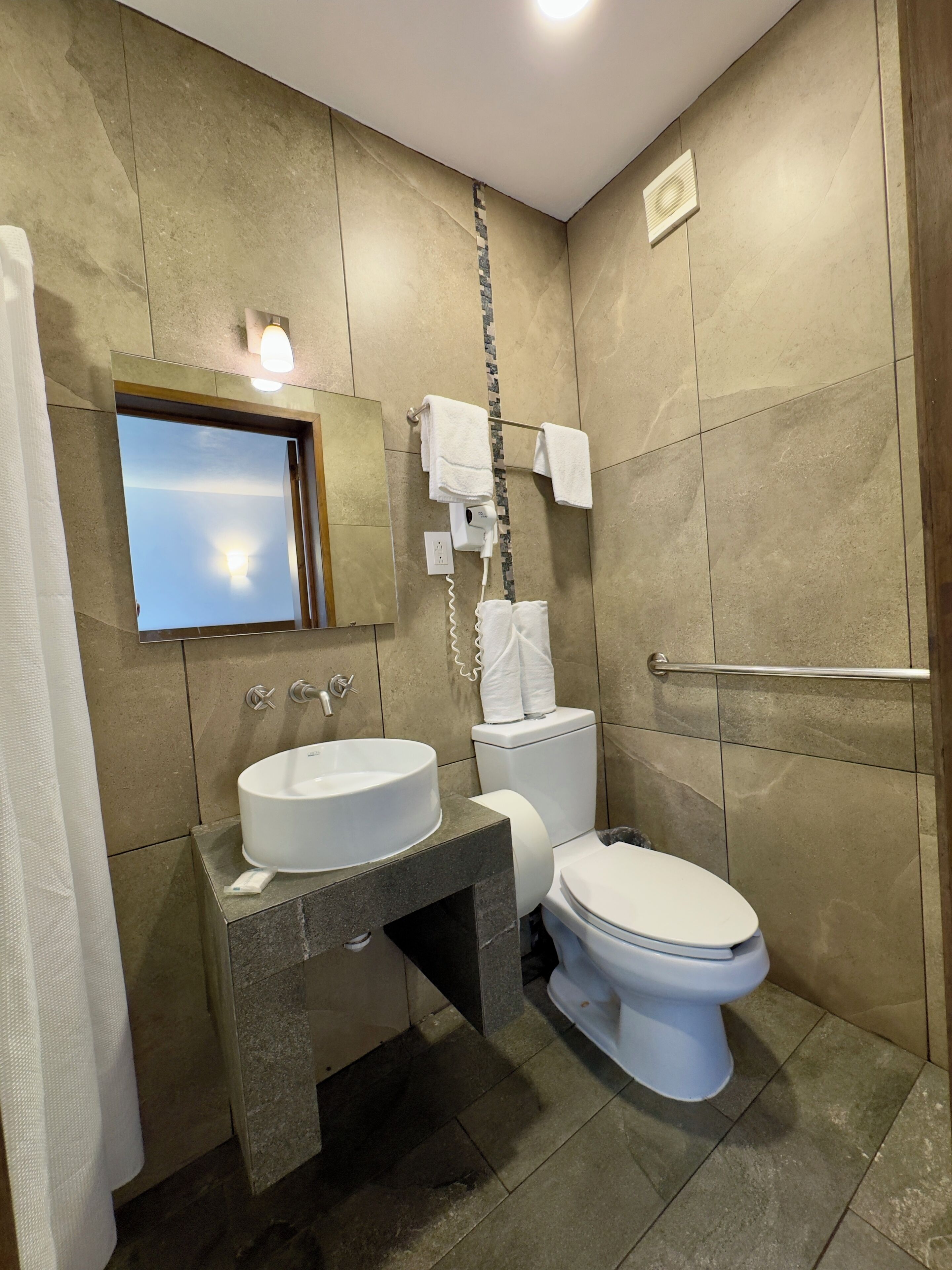 A bathroom with a sink, toilet, and a mirror with a view of the sky.