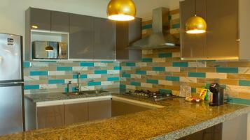 Uma cozinha moderna com eletrodomésticos de aço inoxidável, bancadas de granito e painel de azulejos em tons de verde-água e branco.
