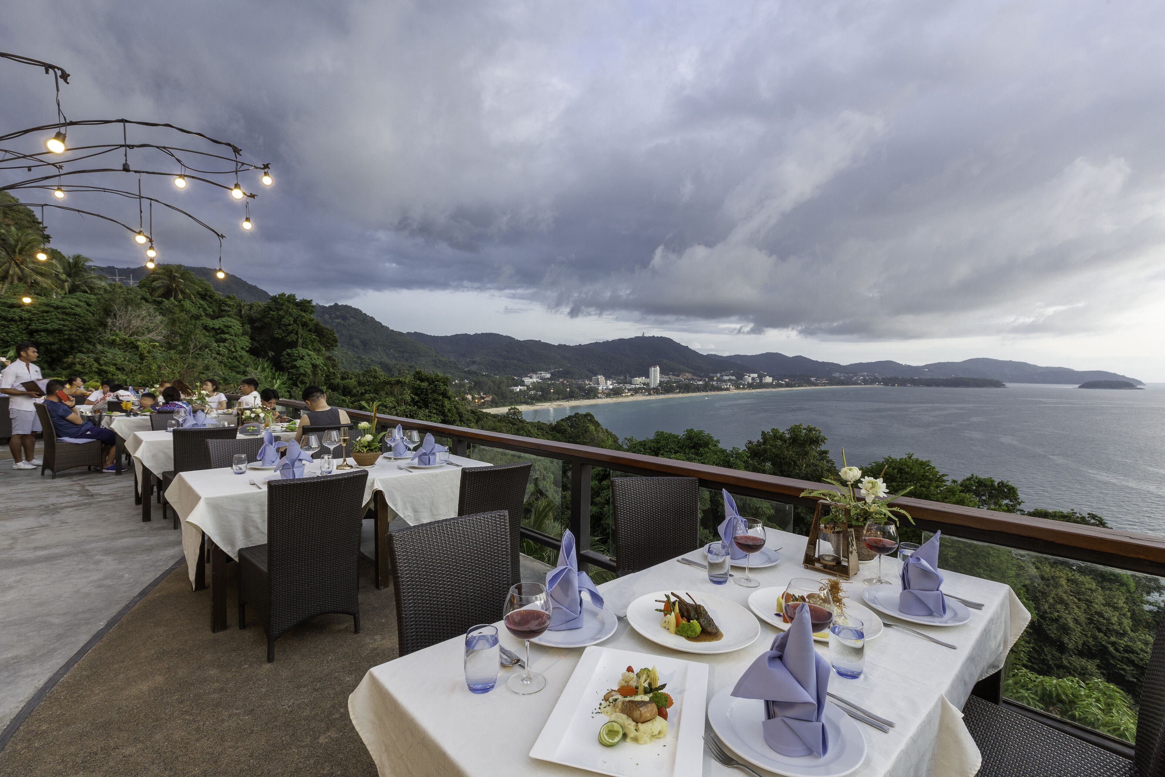 An outdoor dining area with tables set for a meal, overlooking a scenic coastal view.
