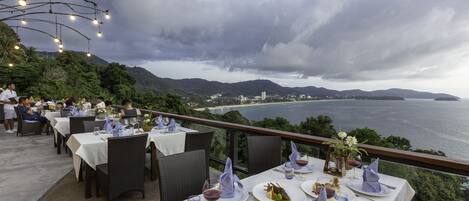 An outdoor dining area with tables set for a meal, overlooking a scenic coastal view.