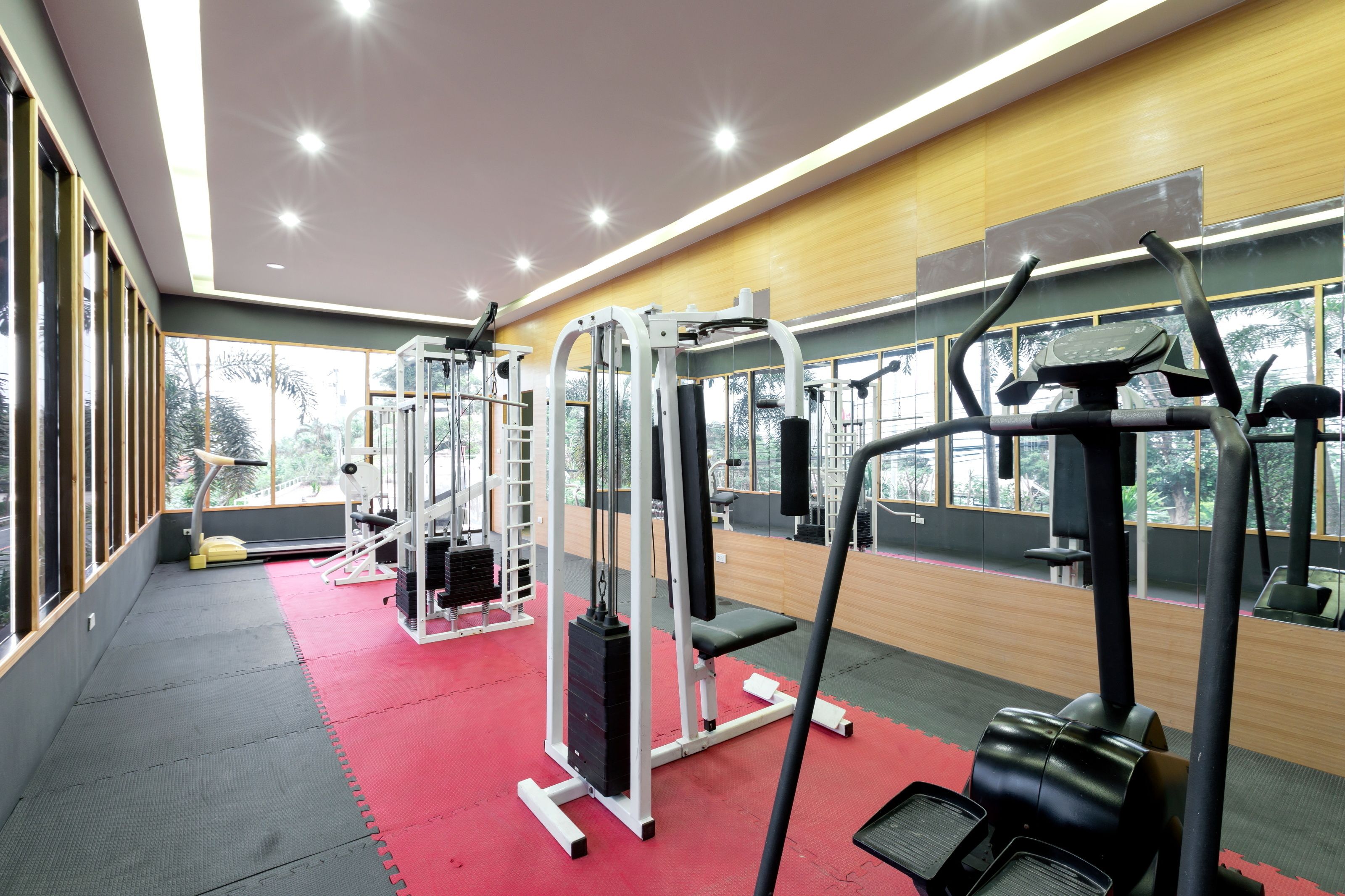 A gym with various exercise machines, large windows, and a red carpeted floor.