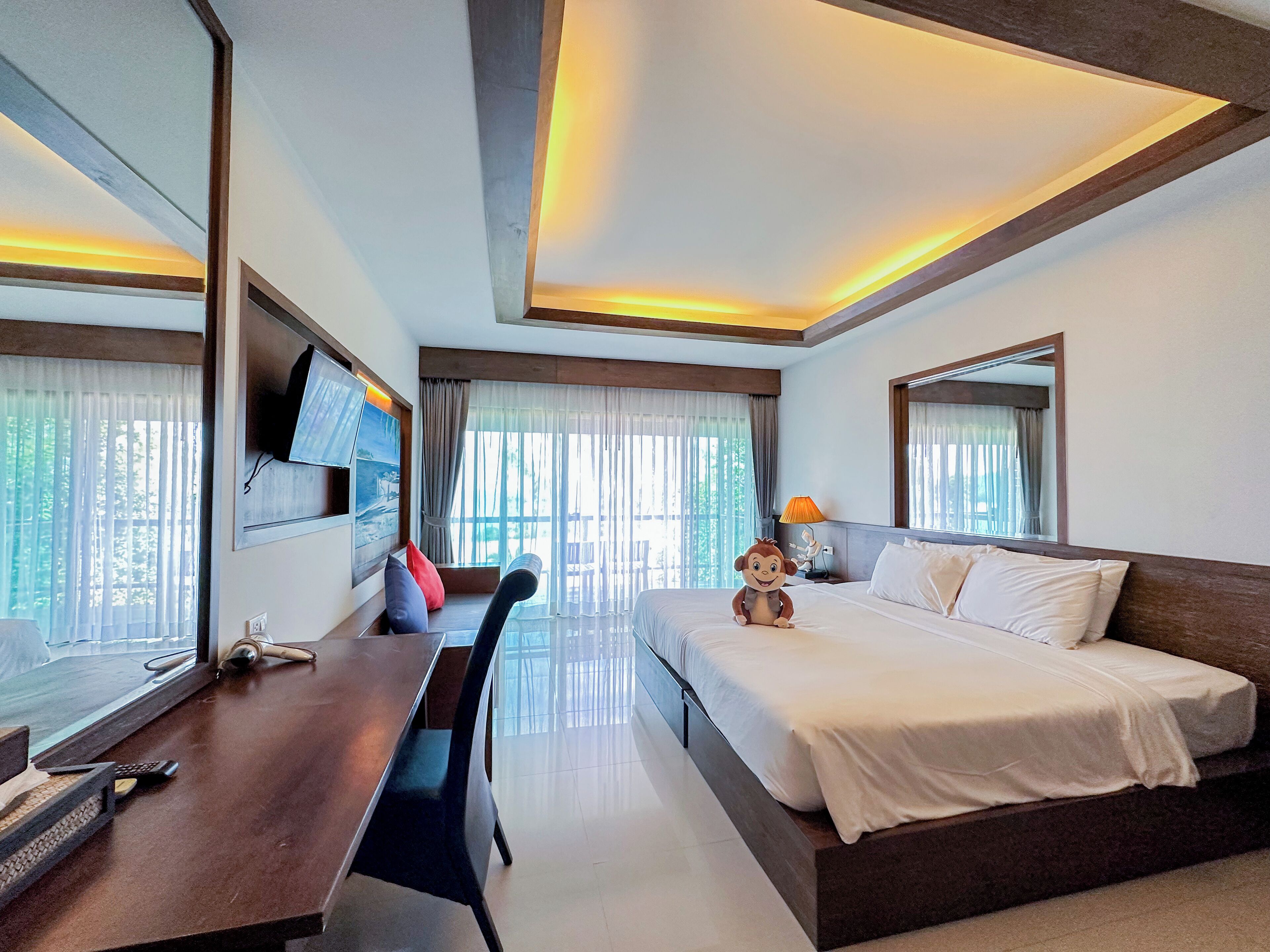 Habitación de hotel con cama, escritorio, silla, televisión y ventana con cortinas.