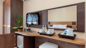 A modern hotel room with a wooden desk, a flat-screen TV, a small refrigerator, a coffee maker, and a potted plant.
