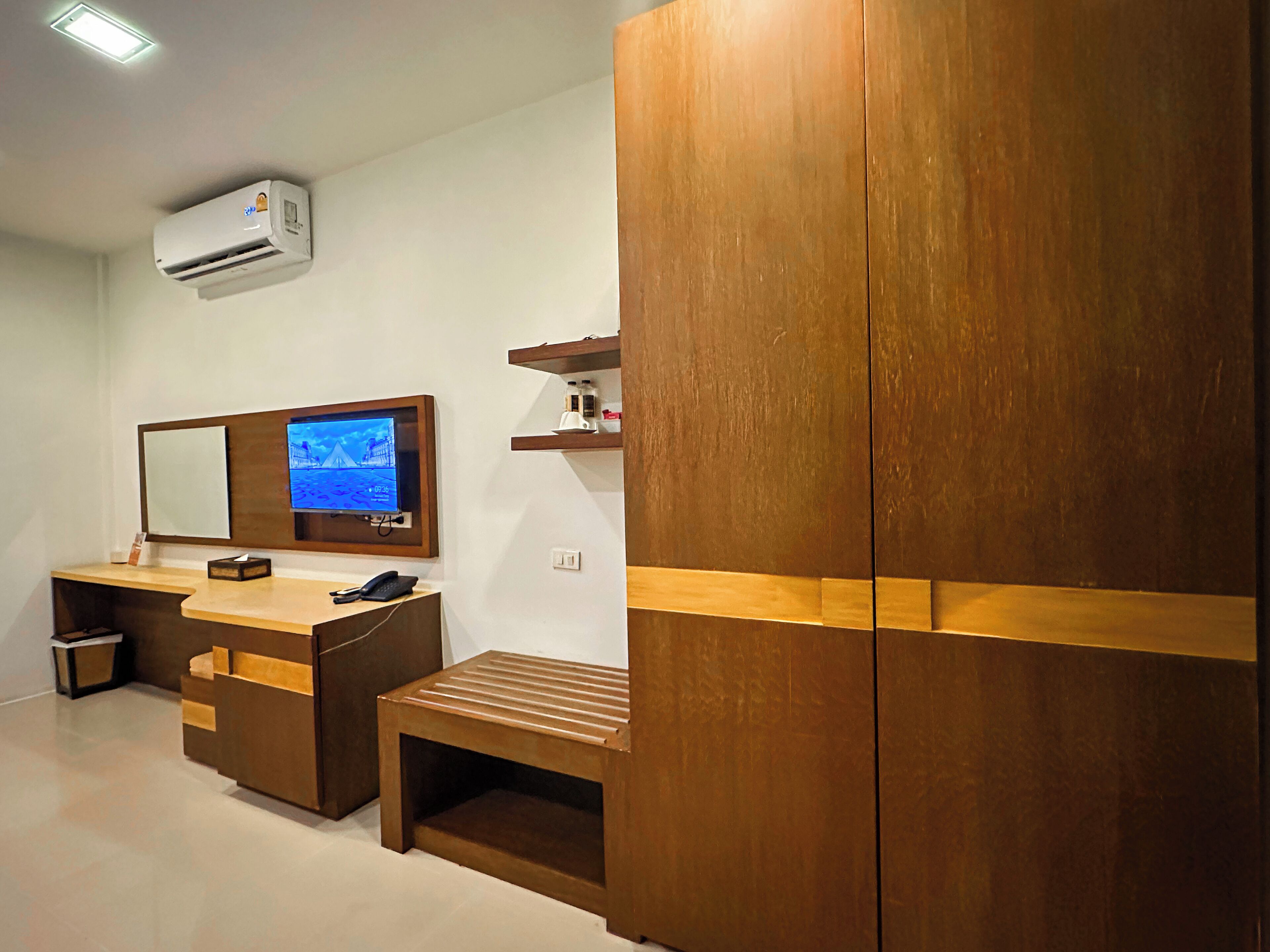 A modern hotel room with a wooden wardrobe, a desk with a telephone, a mirror, and a flat-screen TV.