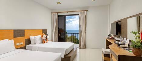 Habitación de hotel con dos camas, un escritorio, un televisor y un balcón con vista al mar.
