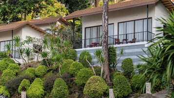 A hotel with multiple-story buildings, a balcony with seating, and a well-maintained garden with various shrubs and trees.