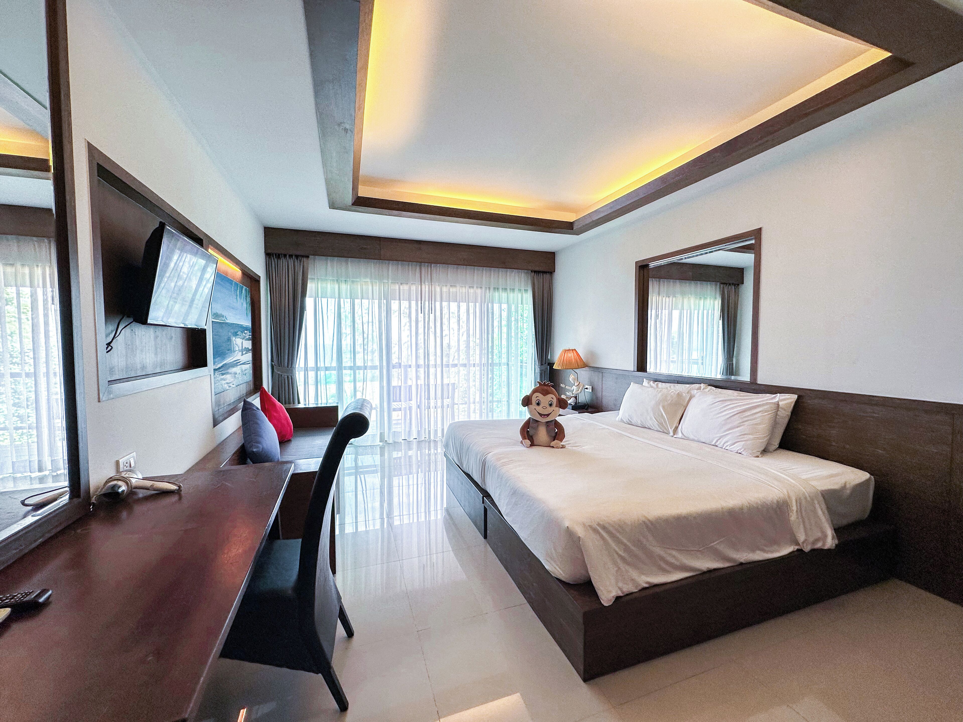 Una habitación de hotel con una cama, un escritorio, una silla, un televisor montado en la pared y un espejo grande.