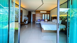 A modern hotel room with a glass door leading to a balcony, a bed with a pillow, a small table with a lamp, and a wall-mounted air conditioner. - Secret Cliff Resort Phuket (Karon)
