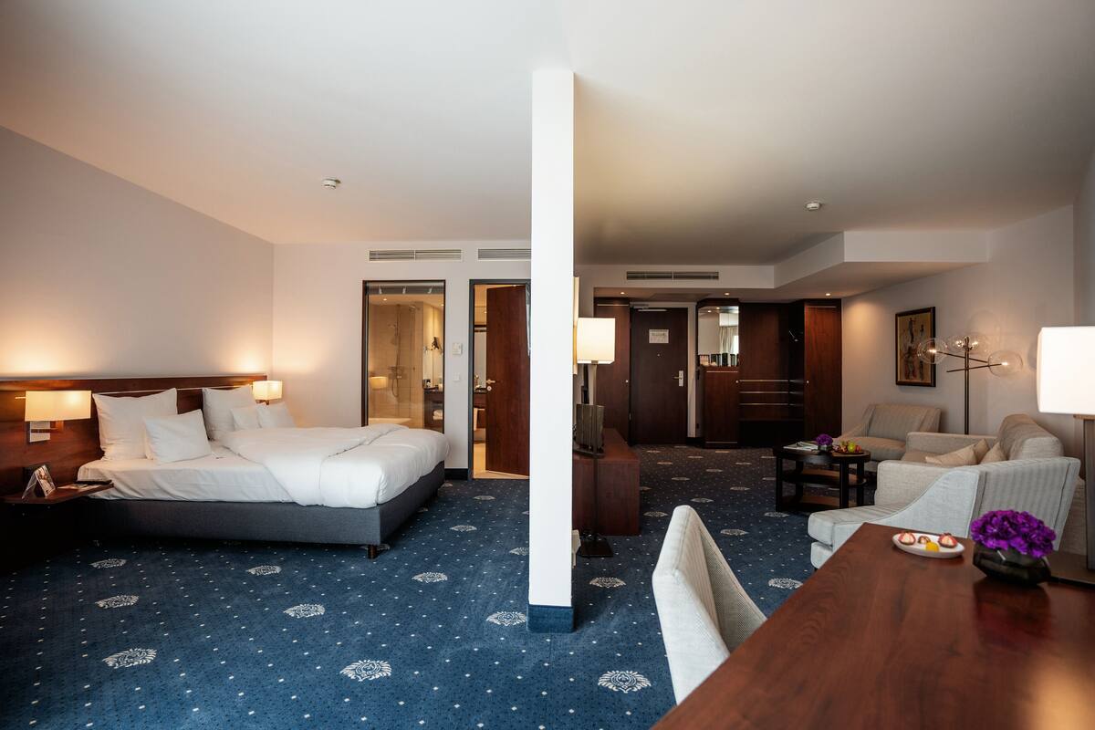 A hotel room with a bed, a desk, a chair, a sofa, and a dining table.