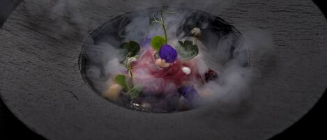 Primer plano de un plato con diversos ingredientes y una flor morada, rodeado de vapor.