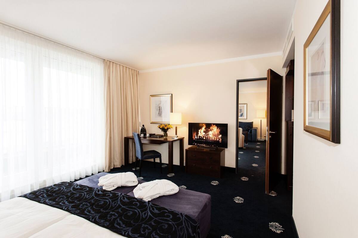 A hotel room with a bed, a desk with a TV, a chair, and a mirror.