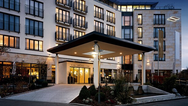 A hotel entrance with a covered outdoor area, multiple balconies, and a well-lit facade. - Hotel Vier Jahreszeiten Starnberg (Starnberg)