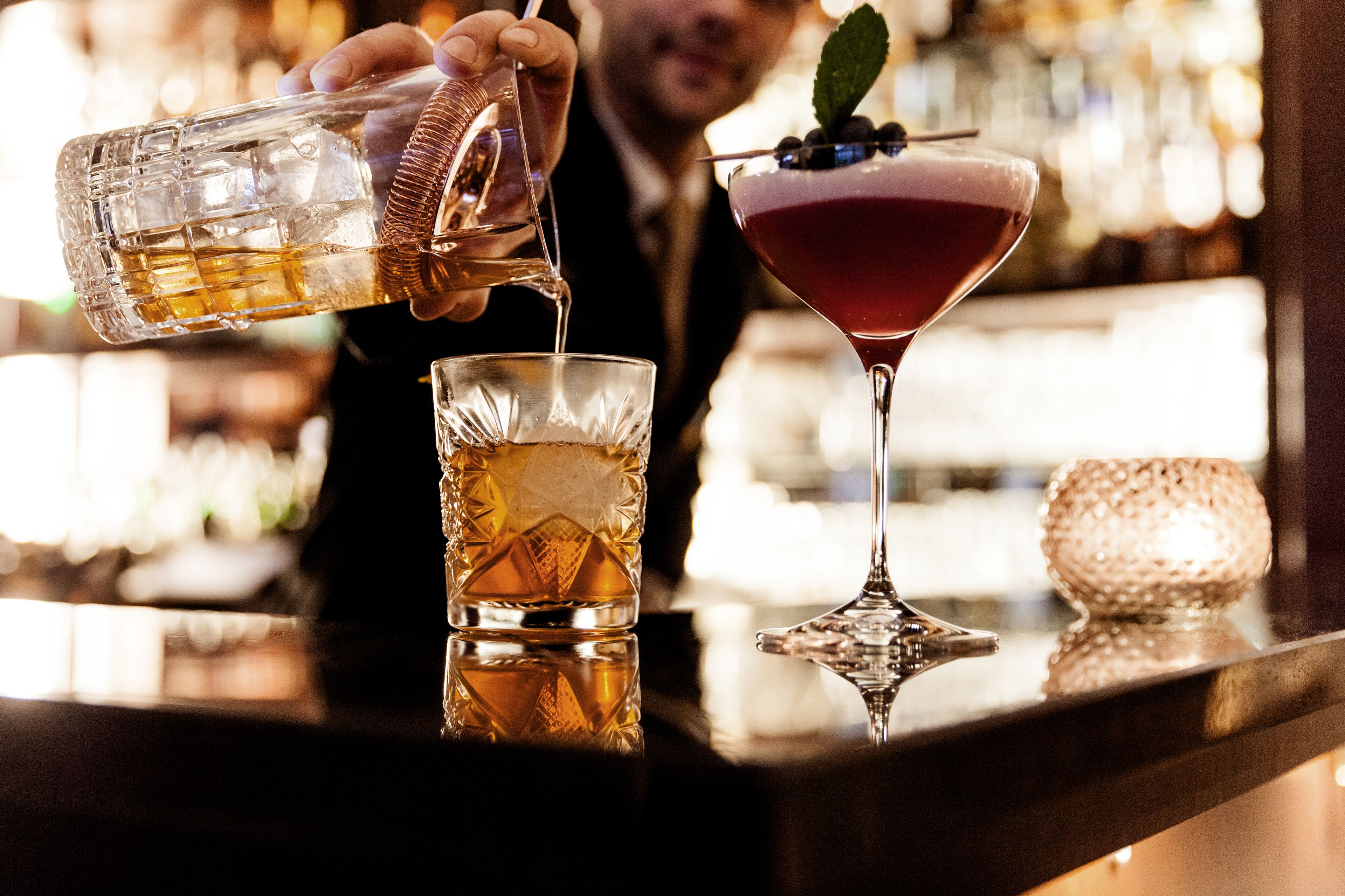 A bartender pouring a drink into a glass.