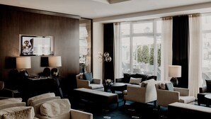 A modern hotel lobby with a seating area, large windows, and a TV mounted on the wall. - Hotel Vier Jahreszeiten Starnberg (Starnberg)