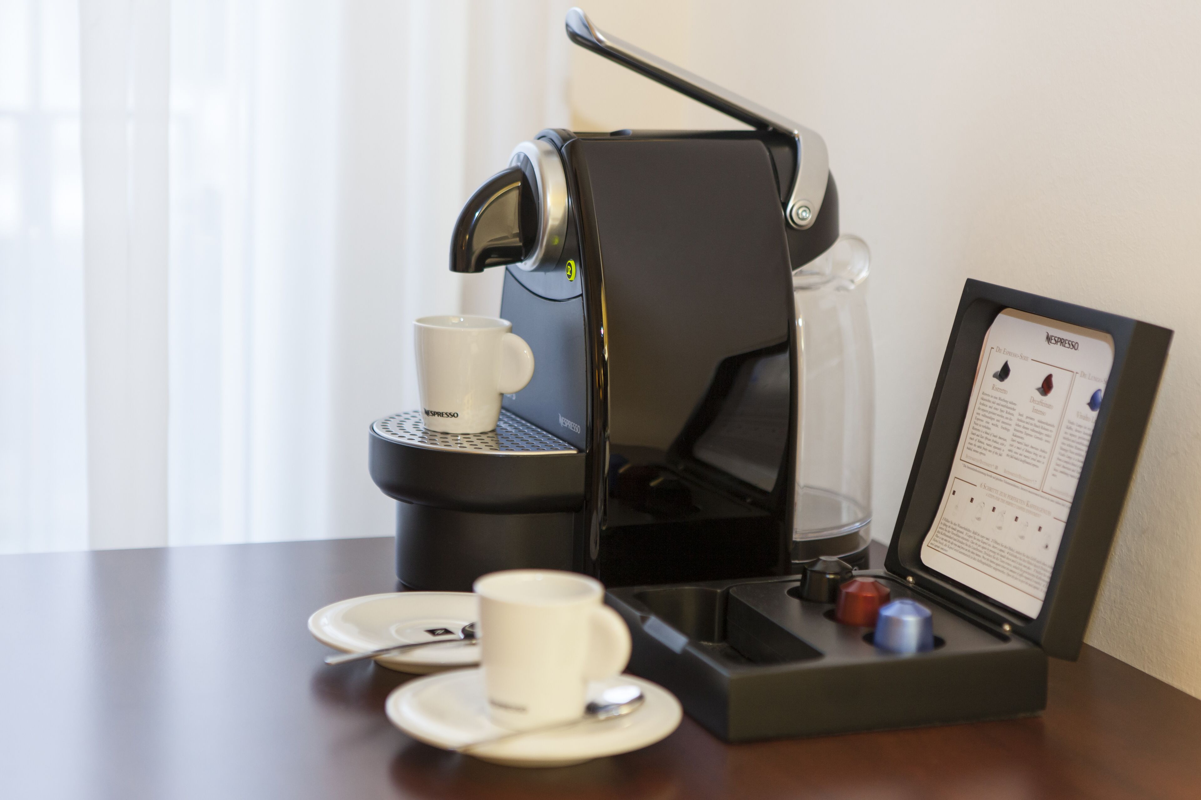A Nespresso coffee machine with a cup and saucer, a glass carafe, and a menu stand.