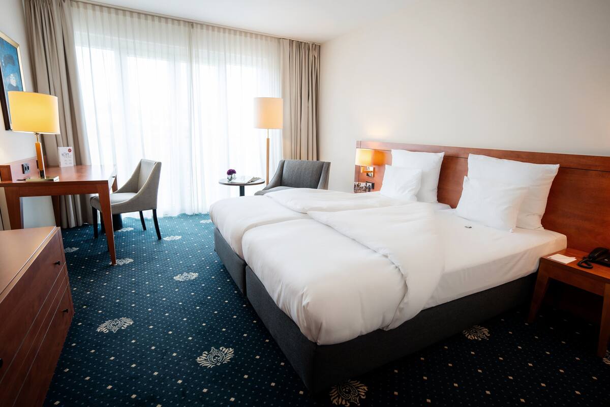 A hotel room with a large bed, two bedside tables, a desk with a chair, and a small table with a lamp.