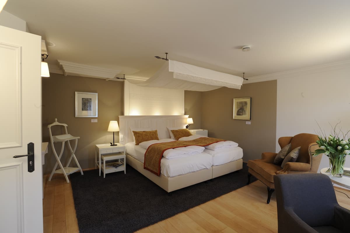 A neatly arranged bedroom with a bed, bedside tables, a chair, and a desk with a vase of flowers.
