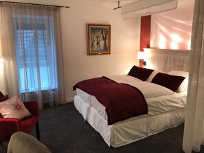 A hotel room with a large bed, a red chair, a small table, and a painting on the wall.