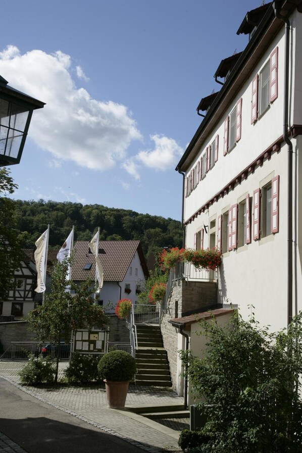 A traditional European building with a staircase leading to a second floor, surrounded by greenery and flags. - Hotel Altes Amtshaus (Mulfingen)