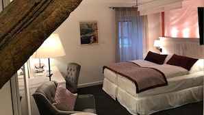 Hotellihuone, jossa on sänky, tuoli, työpöytä, lamppu ja taulu seinällä.