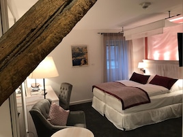 Habitación de hotel con cama, una silla, un escritorio, una lámpara y un cuadro en la pared.