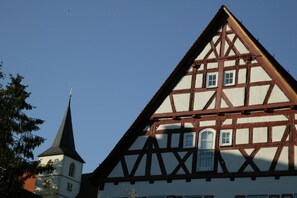 A traditional half-timbered building with a steeply pitched roof and a visible church steeple in the background.