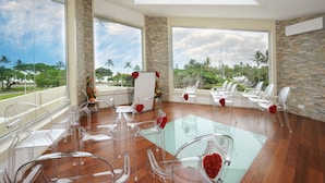 Une pièce spacieuse avec de grandes fenêtres, des chaises transparentes, une table en verre et une vue sur des palmiers et une végétation luxuriante.