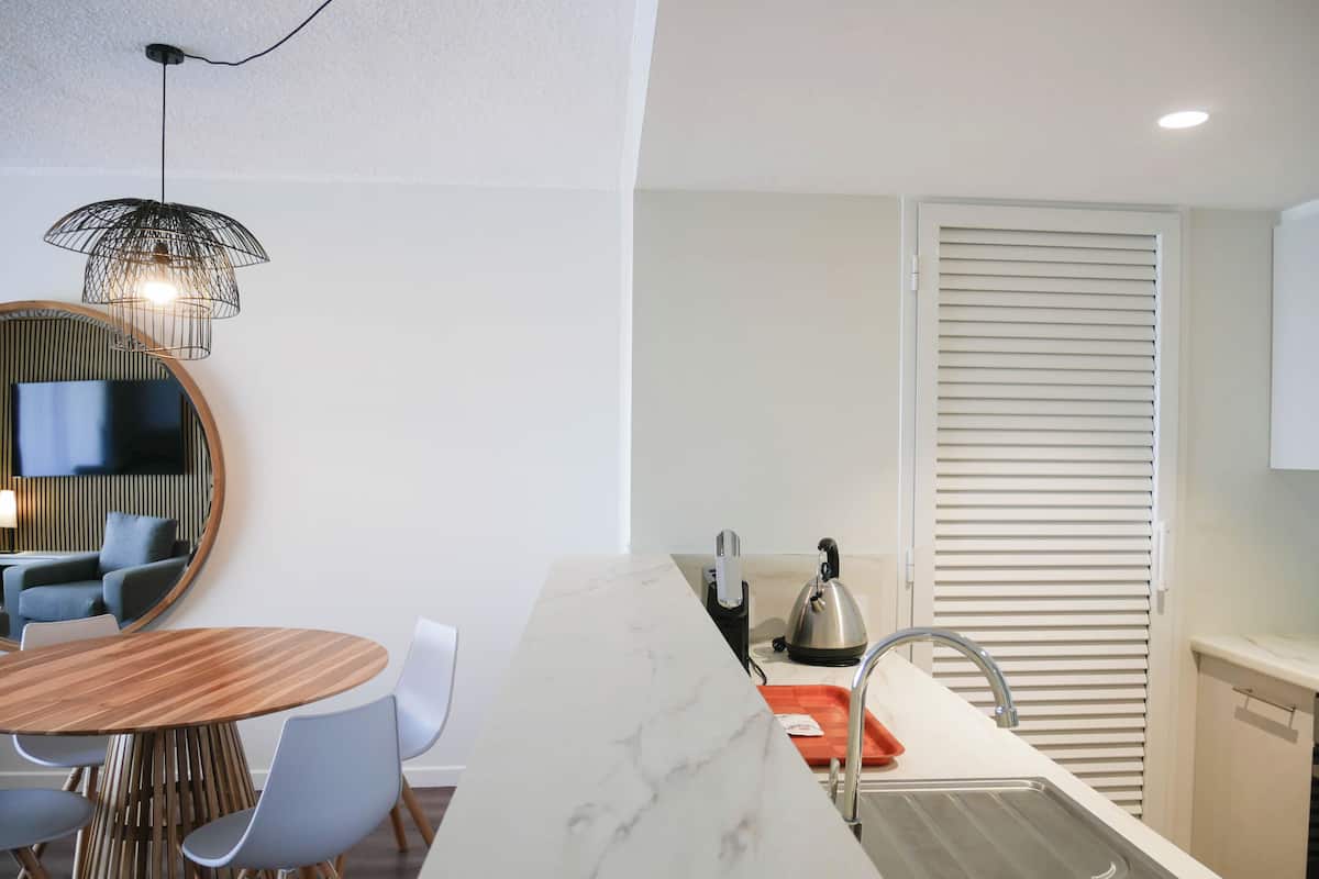 A modern kitchen with a marble countertop, a sink, and a kettle. There is a dining area with a round table and chairs.