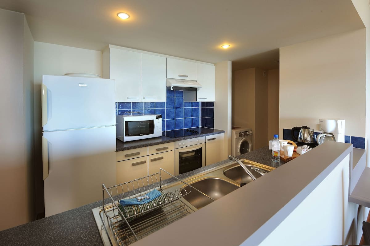 A modern kitchen with white cabinets, a microwave, a sink, and a dish drying rack.