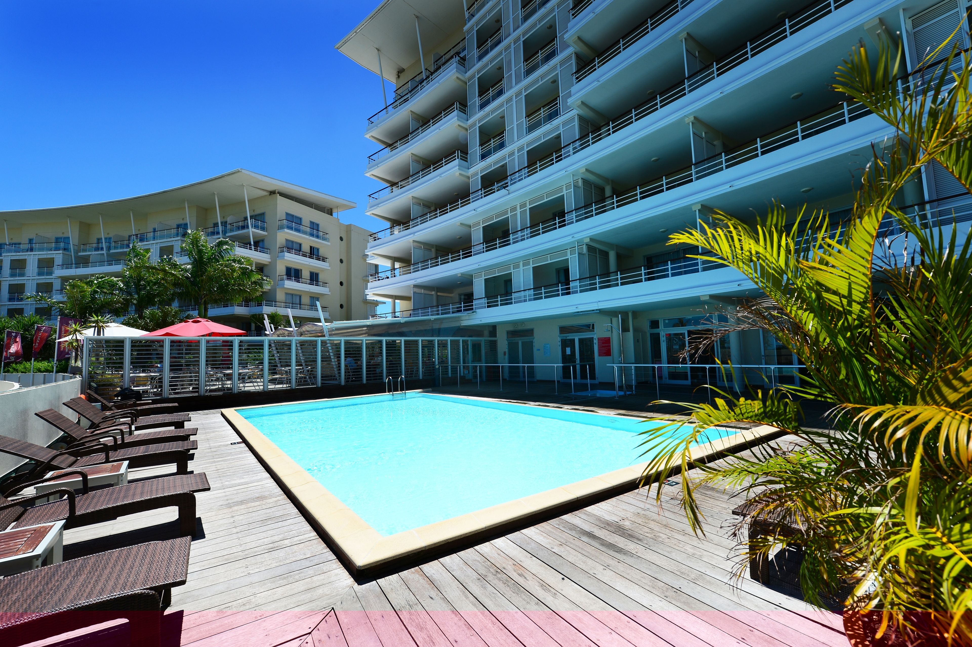 A pool area with lounge chairs and a clear blue pool, surrounded by a multi-story building with balconies.