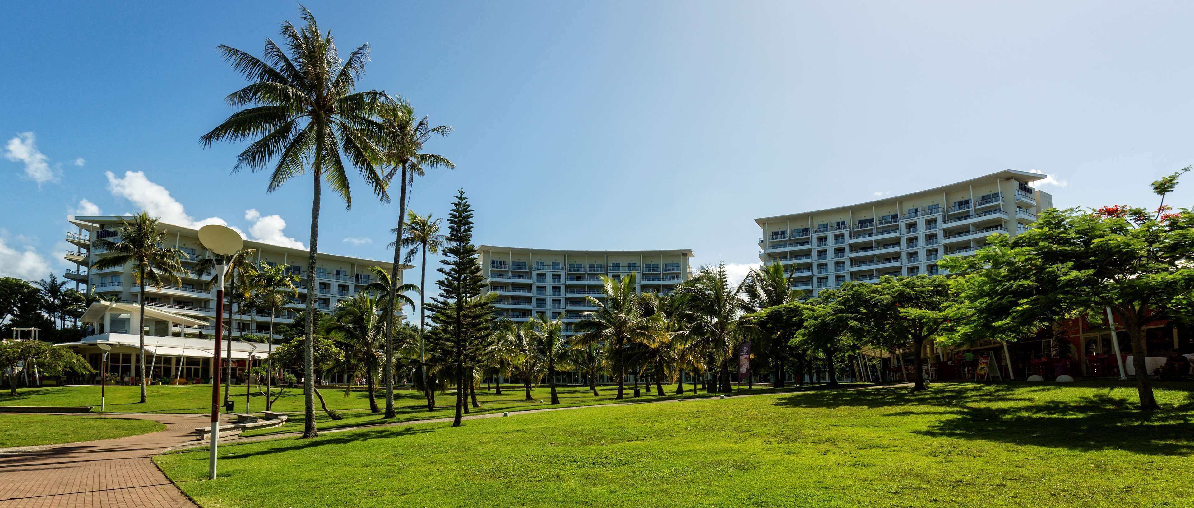 A hotel with multiple floors, a well-maintained lawn, and palm trees.