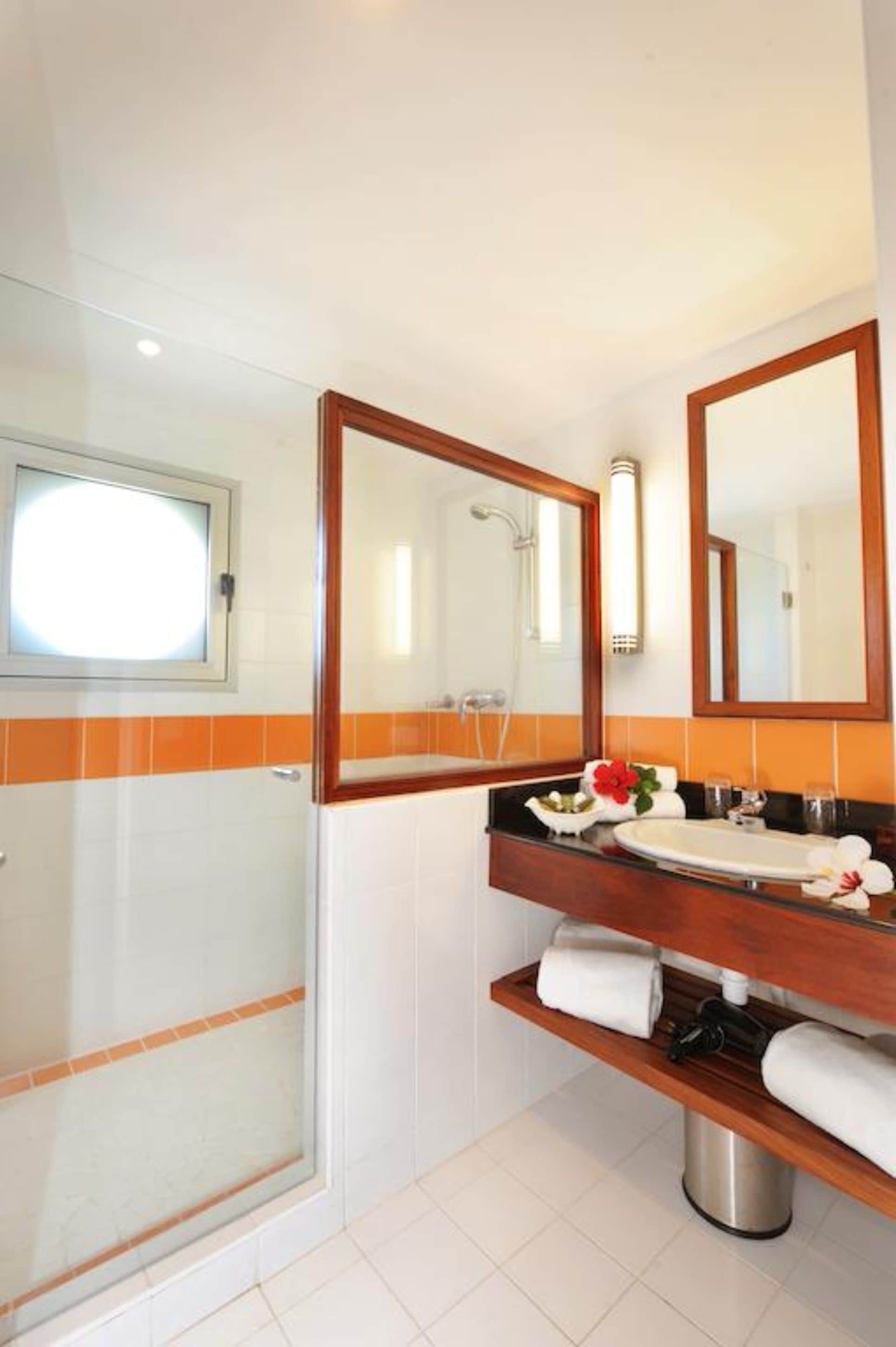 A bathroom with a glass shower enclosure, a wooden vanity with a sink, and a mirror above it.
