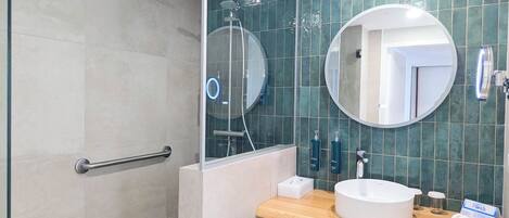 A modern bathroom with a glass-enclosed shower, a round mirror, a wooden vanity, and a towel rack.