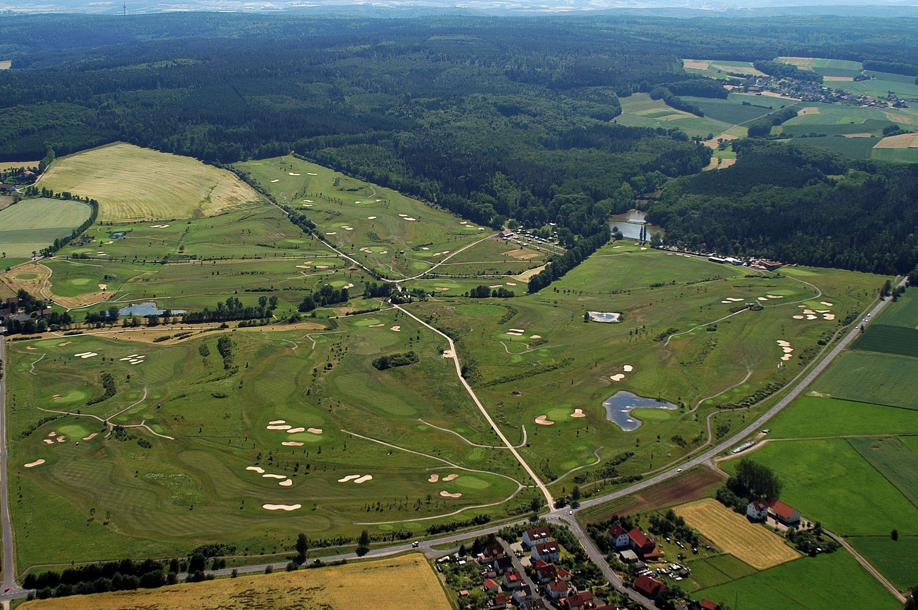 Vista aérea de un campo de golf con varios bunkers, un club de campo y una zona residencial cercana.