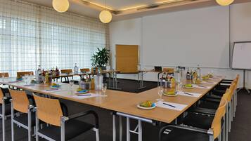 A conference room with a long table, chairs, a projector screen, and a plant.
